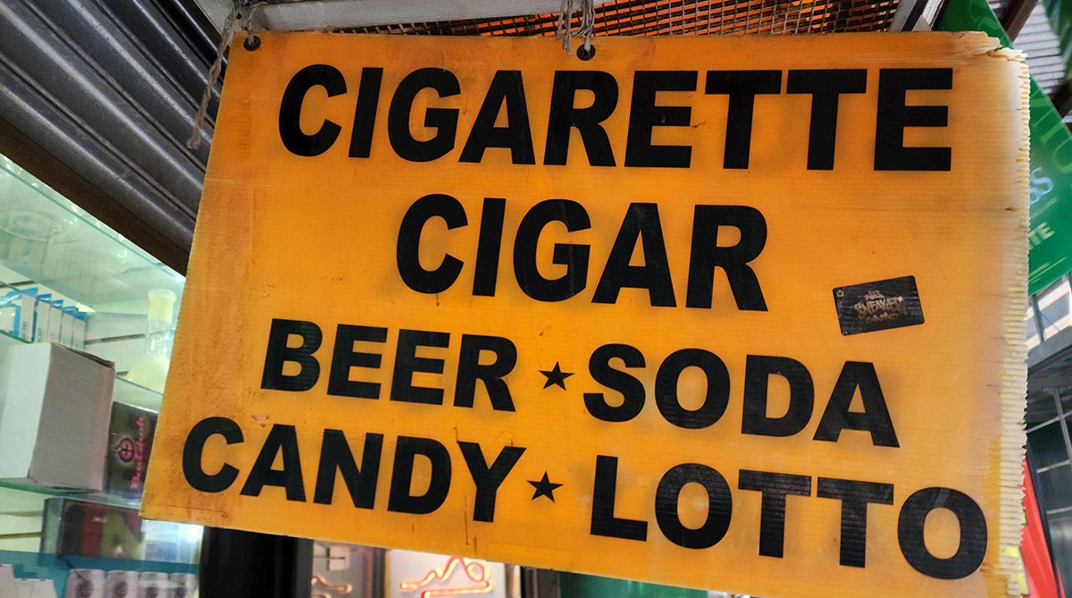 storefront tobacco sign reads, "cigarette, cigar, beer, soda, candy, lotto"